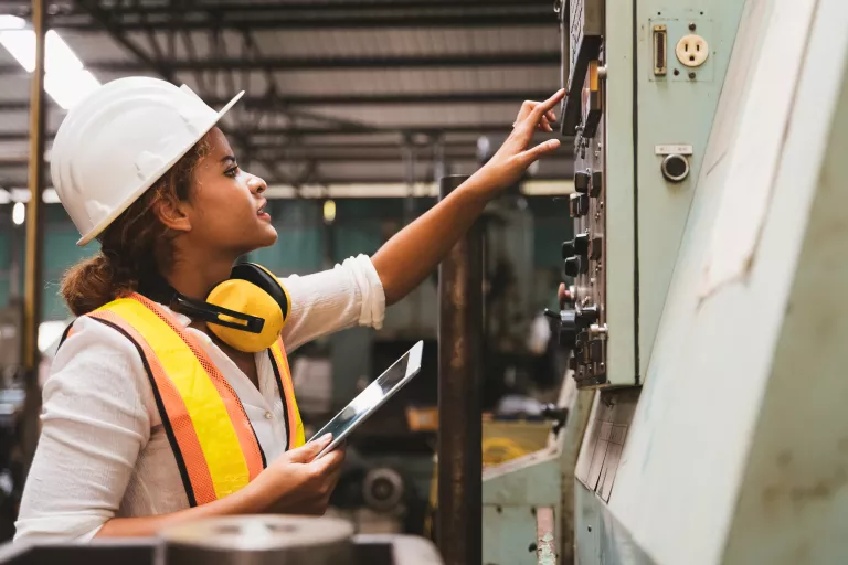 Female maintenance engineer inspecting relay protection system of machinery and holding digital tablet