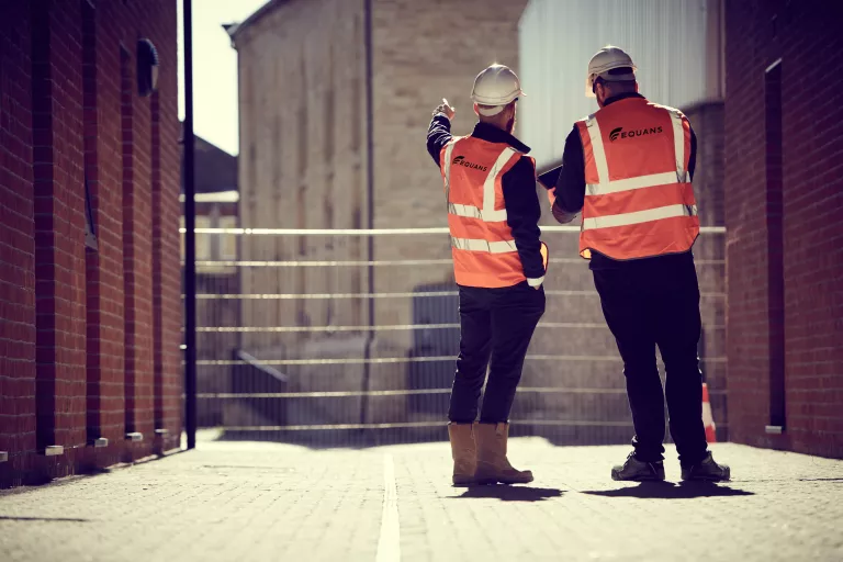 The backs of two Equans employees looking at building