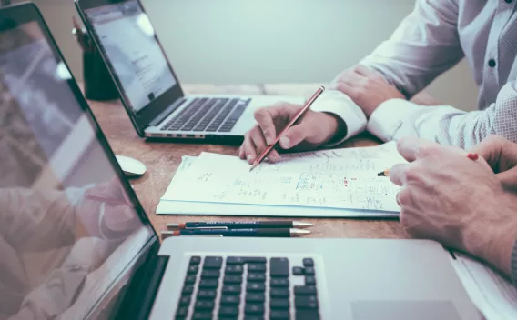 stock image showing co-workers with laptops and workings on a piece of paper