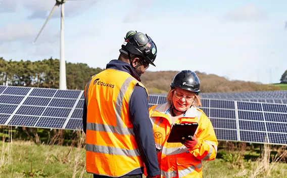 Two Equans employees in front of solar panels looking at ipad