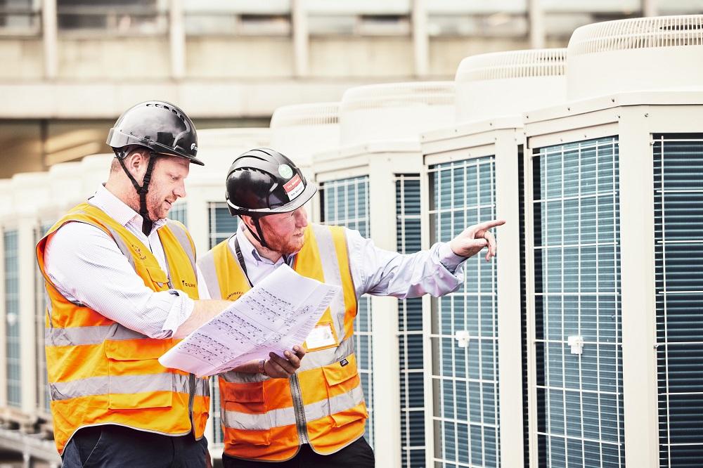 workers on roof next to heat pumps