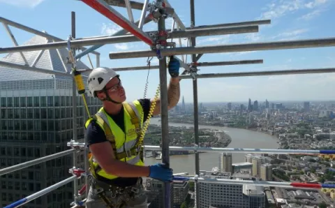 man in hard hat, high vis vest and protective glasses on scaffolding