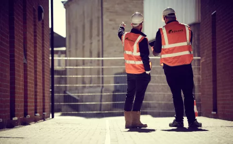 Equans employees from behind stood on a regeneration site in High vis vests and hard hats