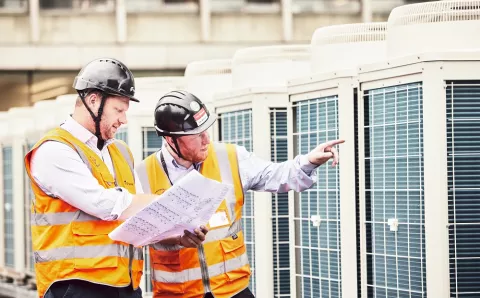 workers on roof next to heat pumps