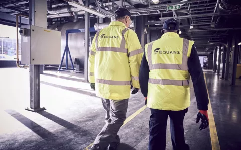 Two Equans workers in a high visability from the back